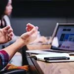 ラップトップを前に説明をする男性と奥にいる女性